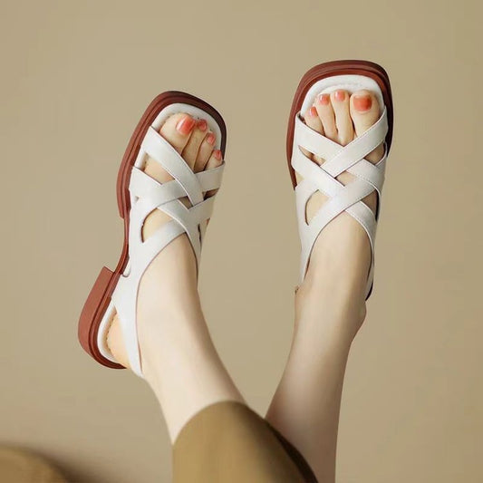 White sandals with brown soles worn by a person on a beige background