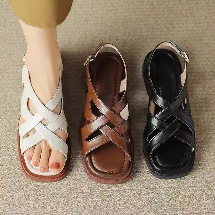 Three sandals in white, brown, and black on a textured surface.